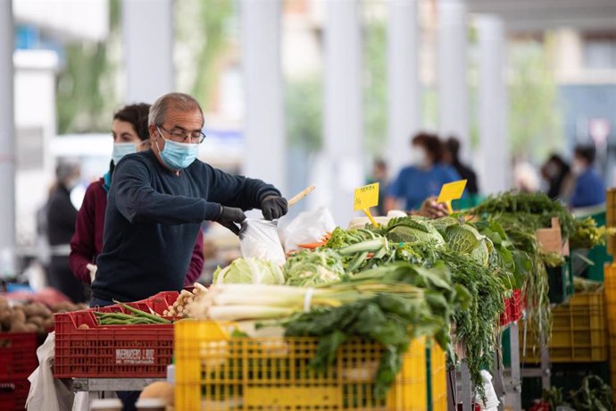 Un hombre con mascarilla despacha verduras en el Mercado de Santa Bárbara (Vitoria)