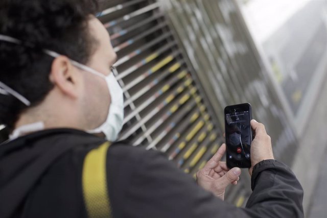 Un hombre protegido con mascarilla realiza una videollamada por su teléfono móvil.