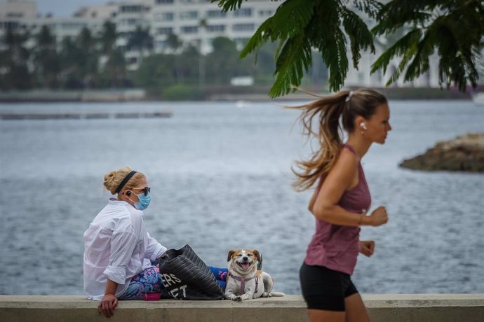 17 April 2020, US, West Palm Beach: A runner jogs past a woman and her dog at the seawall nearby Meyer Amphitheater. Life in Florida continues under the stay-at-home order that will last into May amid the coronavirus pandemic. Photo: Thomas Cordy/Palm B