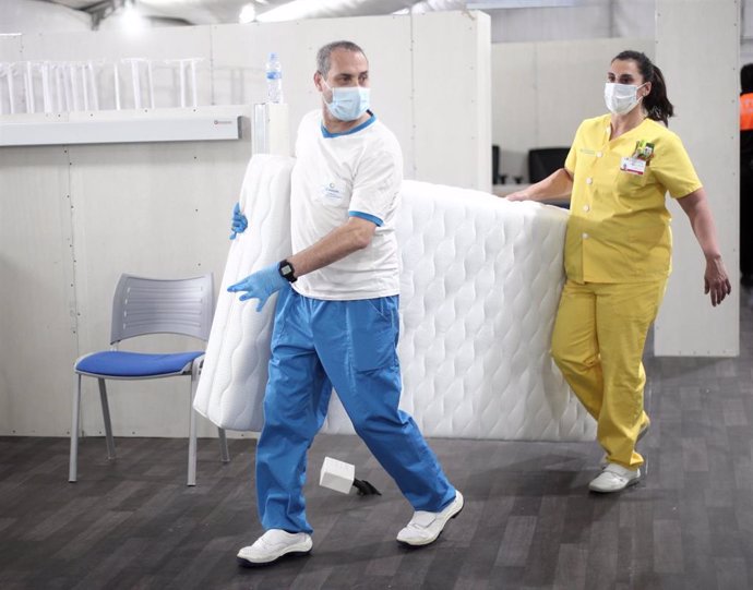 Dos miembros del personal del Hospital de Fuenlabrada trasladan una cama del Hospital de campaña cerca del Hospital de Fuenlabrada.