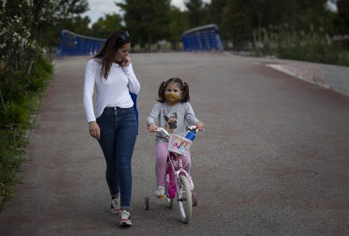 Una mujer con su hija protegida con mascarilla pasean por el parque en el tercer día de desconfinamiento de niños y preadolescentes durante el estado de alarma por la crisis del coronavirus  