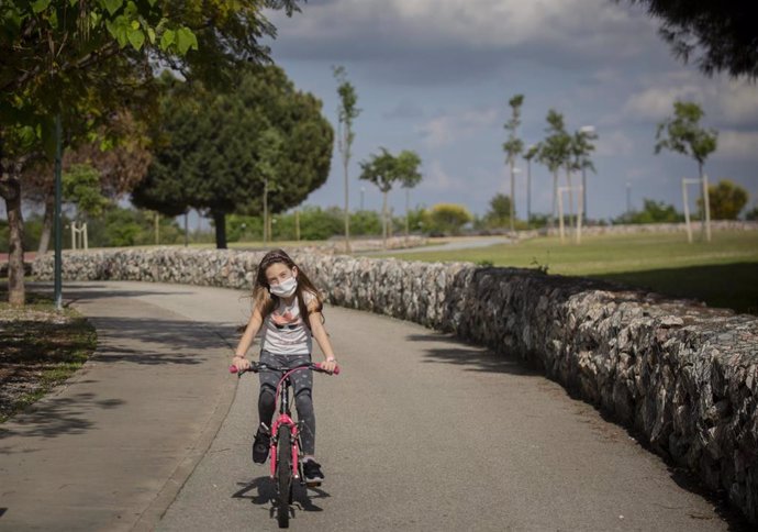 Una niña con mascarilla monta en bicicleta por el parque en el tercer día de desconfinamiento de niños. En Sevilla (Andalucía, España), a 28 de abril de 2020