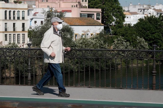 Un hombre mayor pasea por el puente de Triana, en Sevilla, protegido con mascarilla.