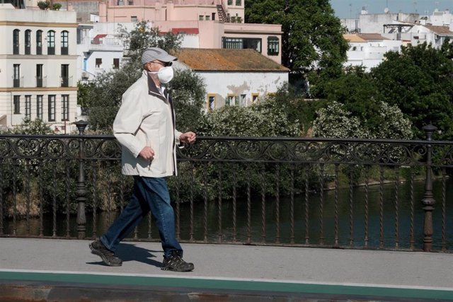 Una persona mayor protegido con mascarilla pasea por un puente.