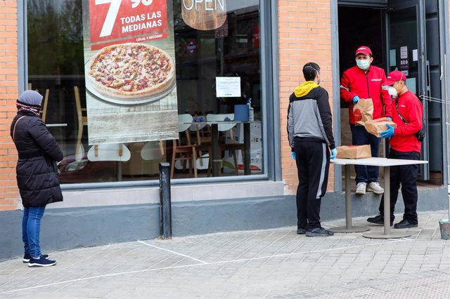 Un hombre protegido con una mascarilla recoge un menú infantil de Telepizza en el barrio de San Fermín en el distrito de Usera