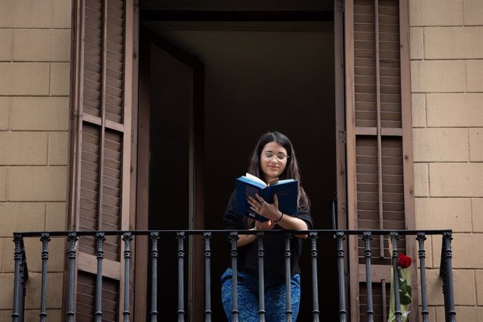 Una joven lee un libro en el balcón de su casa con ocasión de la Diada de Sant Jordi