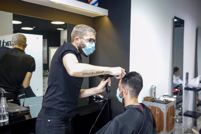 Un empleado de una peluquería atendiendo a un cliente, ambos con mascarilla.