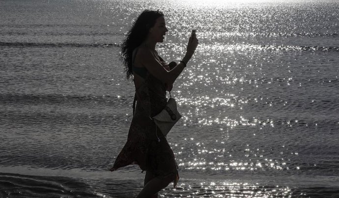 Una mujer mira el móvil en la playa de la Malvarrosa el primer día de salida en Valencia tras 48 días en casa por el coronavirus, en que los adultos pueden salir a pasear y a hacer deporte, en  Valencia / Comunidad Valencia (España), a 2 de mayo de 2020.
