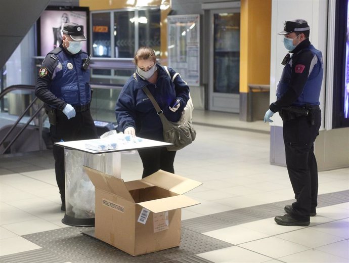 Una pasajera recoge una mascarilla de la mesa que tienen preparada para la entrega agentes de la Policía Municipal de Madrid 
