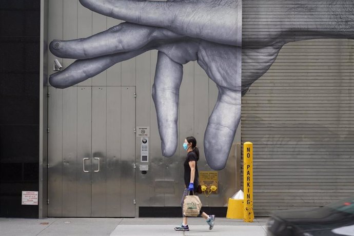 Una mujer con mascarilla paseando ante un mural en Nueva York