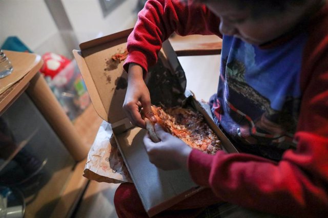 Un niño come un trozo de pizza del menú infantil de Telepizza mientras ve la televisión en su casa.