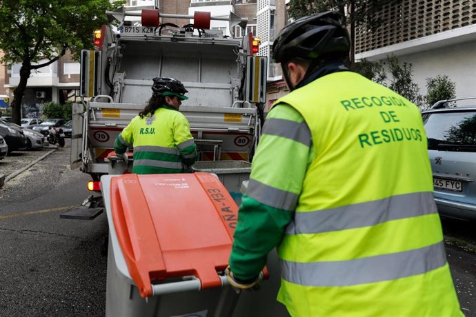 Dos operarios de recogida de residuos protegidos con mascarilla trasladan cubos de basura destinados a desechos para triturar su contenido durante su trabajo de limpieza en una calle de la capital durante el día 33 del estado de alarma, en Madrid (Españ