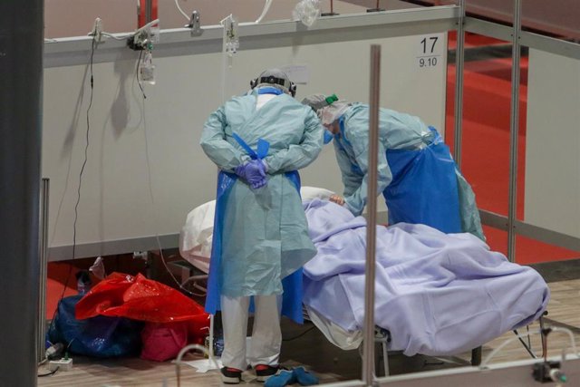 Dos sanitarios protegidos con mascarilla y gorro atienden a un paciente con coronavirus en el Hospital temporal de la Comunidad de Madrid habilitado en IFEMA, en Madrid (España) a 31 de marzo de 2020.