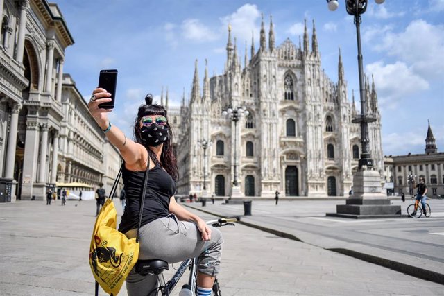 Una mujer con mascarilla se hace un selfie frente a la catedral de Milán