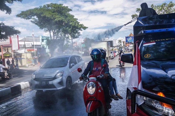 Un equipo de Policía de Indonesia rocía con desinfectante un coche circulando por una calle de Makassar