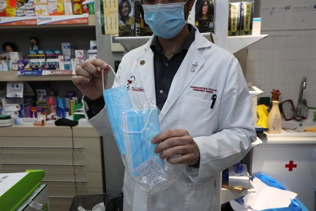 Un farmacéutico muestra una de las mascarillas que se venden en su farmacia