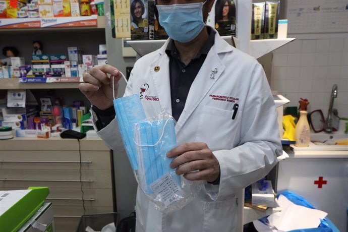 Un farmacéutico muestra una de las mascarillas que se venden en su farmacia