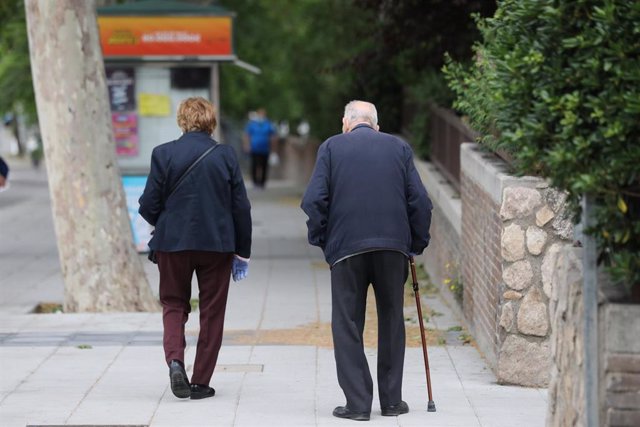 Una mujer de edad avanzada pasa al lado de un hombre con bastón que pasea por la capital en su franja horaria permitida