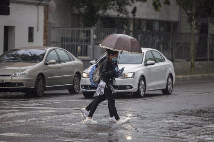 Dos personas cruzan un charco de agua durante la alerta amarilla por lluvia. En el estado de alarma por la crisis del coronavirus, (Covid-19). En Sevilla, (Andalucía, España), a 27 de abril de 2020.