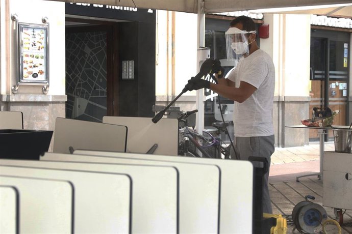 Un trabajdor desinfecta el mobiliario de la cafetería