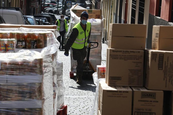 Militares de la Guardia Real protegidos con guantes y mascarillas empujan por una calle un carro con las cajas de alimentos que han recogido en el Banco de Alimentos de Madrid.