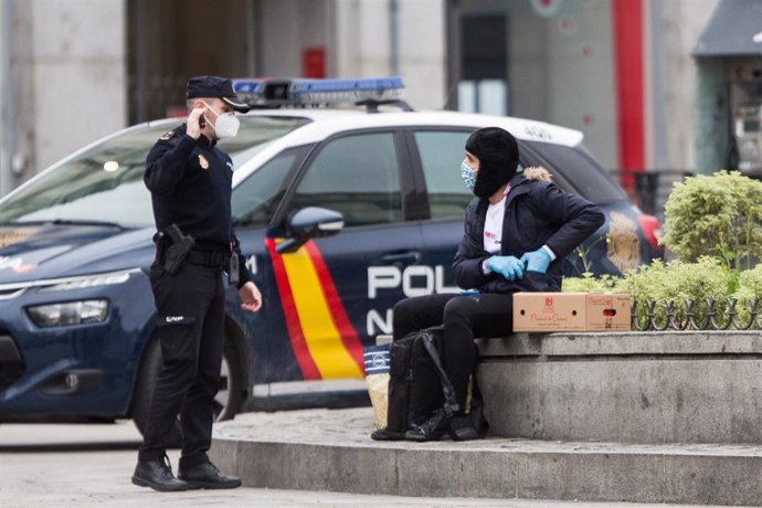 Un policía nacional habla con un hombre sentado en las inmediaciones de la Puerta del Sol 