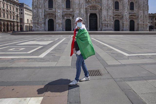 Un hombre con la bandera de Italia y mascarilla frente a la catedral de Milán