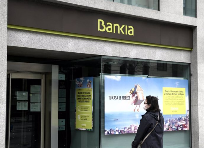 Una mujer con mascarilla espera con un perro frente a una sucursal de Bankia.