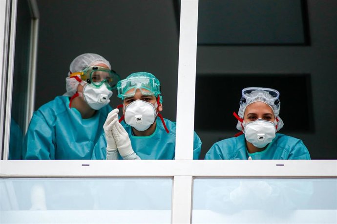 Varios sanitarios con protección EPI, mascarillas, gafas y guantes saludan desde una ventana del Hospital de la Fundación Jiménez Díaz, en Madrid.