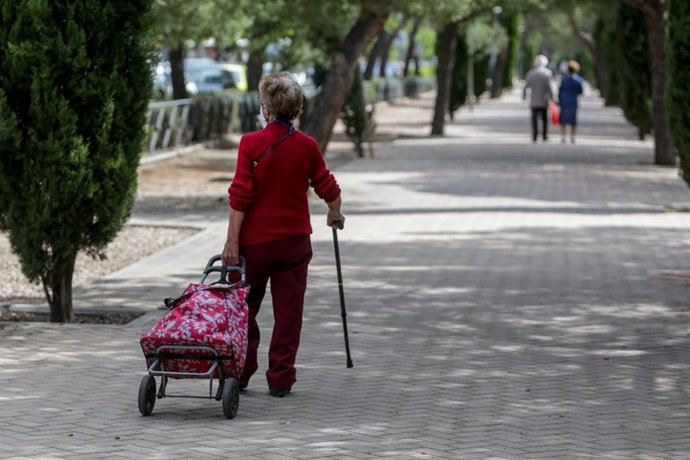 Una mujer en la calle con mascarilla, un bastón y un carrito de la compra 