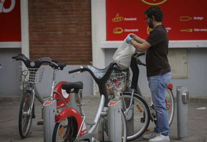 Un hombre deposita una bolsa en una bicicleta del servicio Sevici reactivado para permitir desplazamientos permitidos en estado de alarma en Sevilla