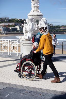 Un hombre lleva a otro en silla de ruedas en el día en que el Gobierno permite salir a hacer deporte de forma individual , en San Sebastián, a 2 de mayo de 2020.