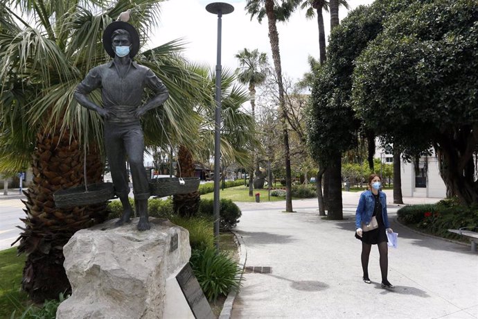 Una persona pasa por delante de la escultura de El Cenachero ataviado con una mascarilla durante el Estado de Alarma por el COVID-19. Málaga a 21 de abril del 2020