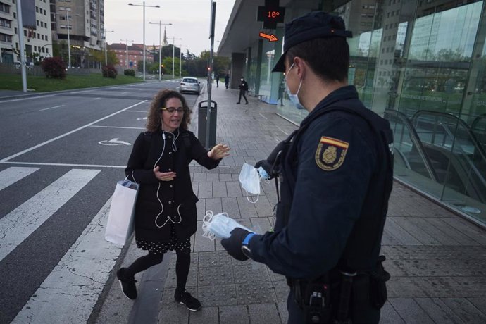 Un policía nacional entrega una mascarilla a una mujer en una calle de Pamplona el día en el que se reactiva la actividad laboral no esencial en Navarra en las empresas cuyos empleados no puedan teletrabajar cuando se cumple un mes desde el inicio del e