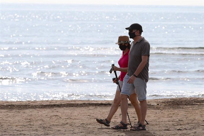 Dos personas protegidas con mascarilla pasean por la playa de la Malvarrosa durante su franja horaria permitida en la desescalada ante la crisis del Covid-19 en la que mayores de 14 años y menores de 69 tienen permitidas las salidas para pasear y hacer 
