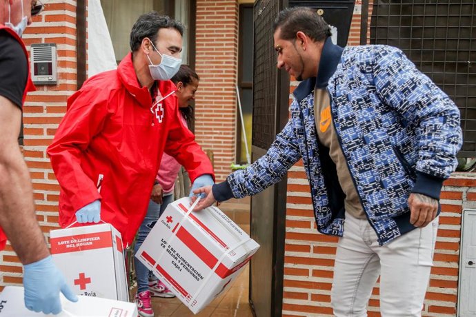 Dos voluntarios de la Unidad de Respuesta Social de la Cruz Roja (URS) entregan a una pareja en su domicilio uno de los kits de ayuda 