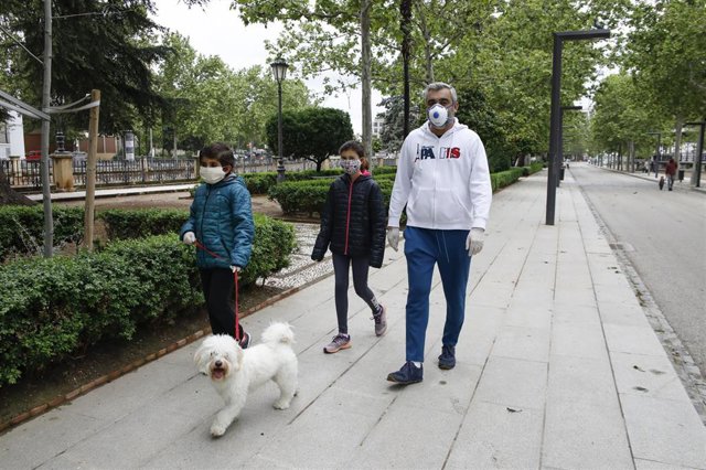Dos niños con mascarillas acompañados por su padre pasean al perro , el primer día en el que los menores de 14 años pueden salir a la calle durante el estado de alarma por la crisis del coronavirus en el país. En Granada, a 26 de abril de 2020.