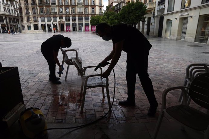 Trabajadores de la cafetería Central ubicada en la Plaza de La Constitución, en Málaga se afanan en la limpieza de los enseres de la terraza 