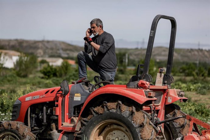 Un hombre habla por teléfono montado en un tractor para segar la tierra del campo, foto de archivo