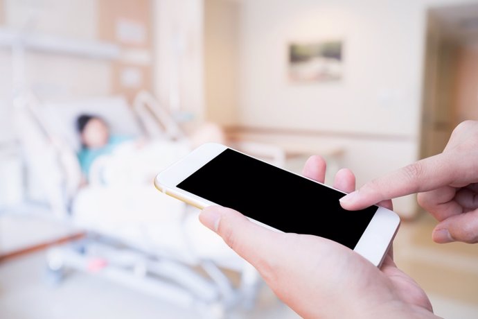 Mano femenina sosteniendo teléfono móvil inteligente con sala de hospital paciente COVID-19