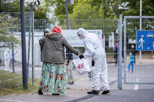 Un agente de seguridad con traje de protección examina una bolsa de una mujer en la entrada de un centro para refugiados en Alemania