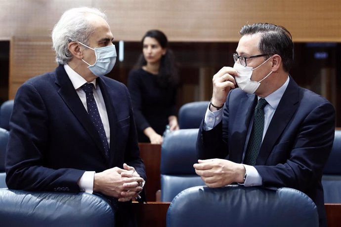 El consejero de Sanidad, Enrique Ruiz Escudero (i), conversa con el portavoz del PP, Alfonso Serrano, durante la sesión de control al ejecutivo regional en la Asamblea de Madrid.