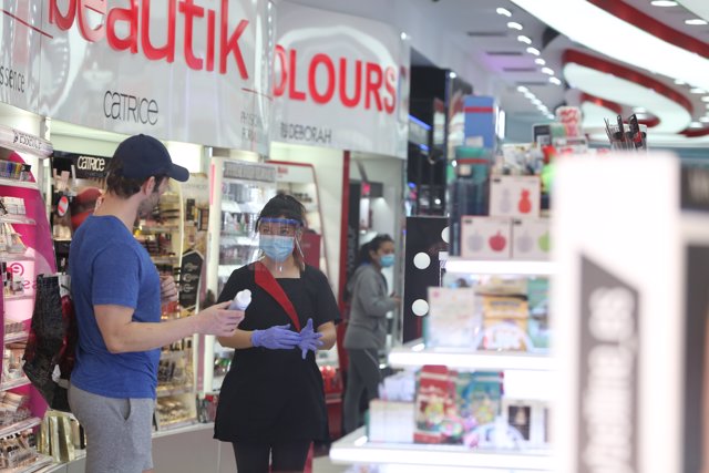 Una trabajadora protegida con una pantalla protectora atiende a un cliente en una tienda de cosméticos. En Madrid (España), a 18 de mayo de 2020.