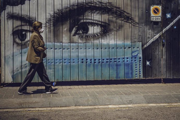 18 May 2020, Spain, Barcelona: A woman with a face mask walks past a graffiti by the city artist Shafir, which depicts a person with a mouth guard. Photo: Matthias Oesterle/ZUMA Wire/dpa