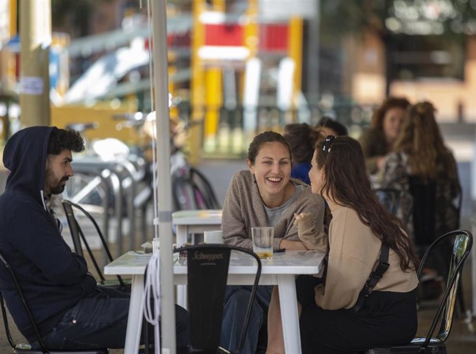 Un grupo de personas sentadas en los veladores de un bar, el día en el Sevilla pasa a la fase la fase 1 del plan de desescalada