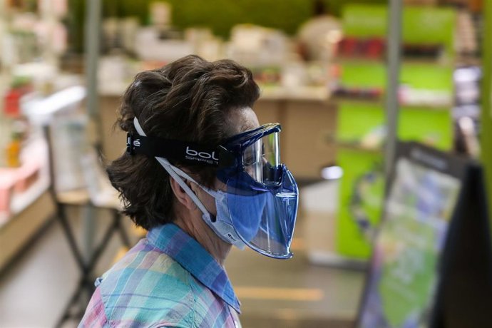 Una mujer protegida con mascarilla y gafas protectoras pasa junto a una tienda abierta después de que el Ministerio de Sanidad autorizara a que la totalidad de la Comunidad Valenciana pasase en su conjunto a la fase 1 de la desescalada