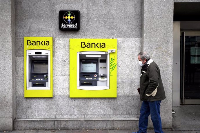 Un hombre con mascarilla pasa por delante de un cajero de Bankia.