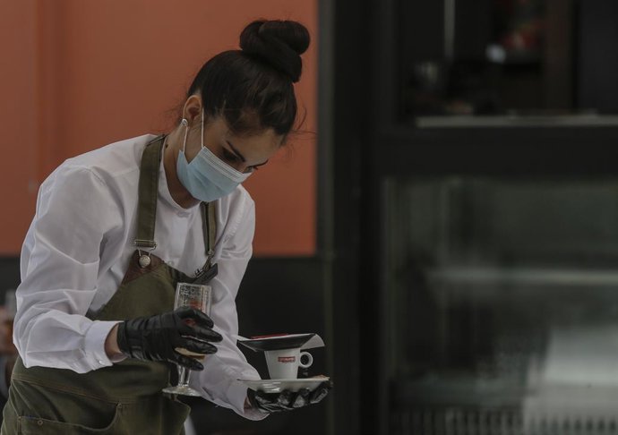 Una camarera con mascarilla y guantes atiende un bar