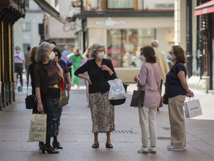 Varias personas protegidas con mascarillas conversan en una calle.