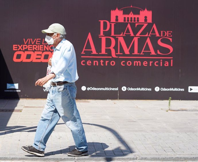 Un ciudadano pasea con mascarilla delante de un cartel de un centro comercial  en la segunda semana de la fase 1 en Sevilla a 20 de mayo del 2020